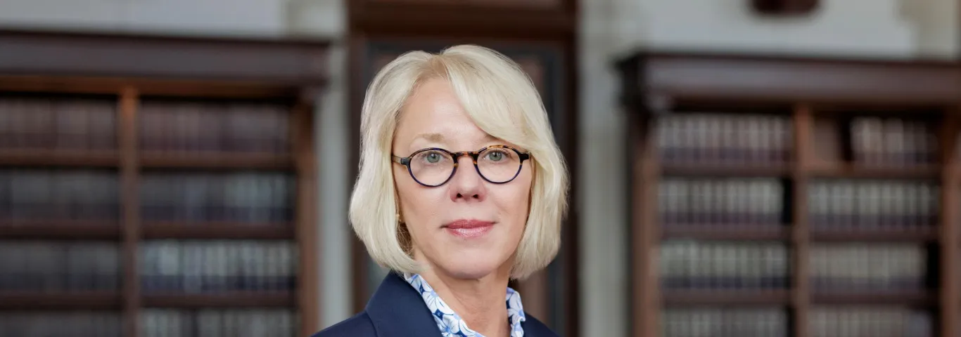 Photo of Law Dean Stephanie Lindquist looking at camera in a library wearing a blue blazer and blue patterned button up shirt