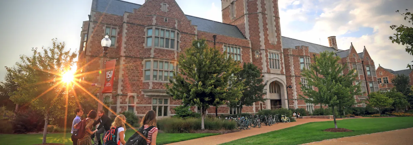 Students with backpacks walk towards Seigle hall at sunset.