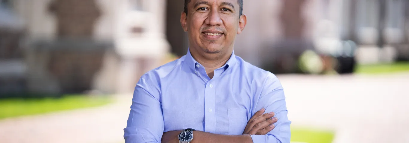 Photo of Ted Enamorado smiling in a light colored shirt with arms crossed on WashU's campus