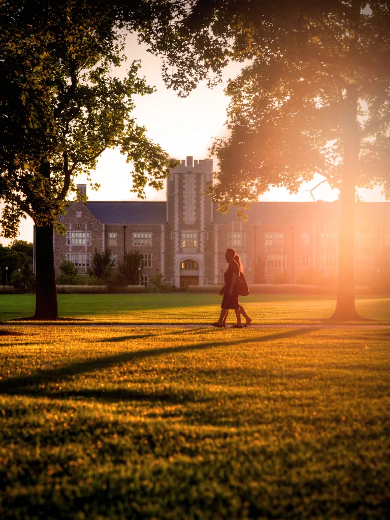 People walk in front of Seigle Hall at dusk across Mudd Field.